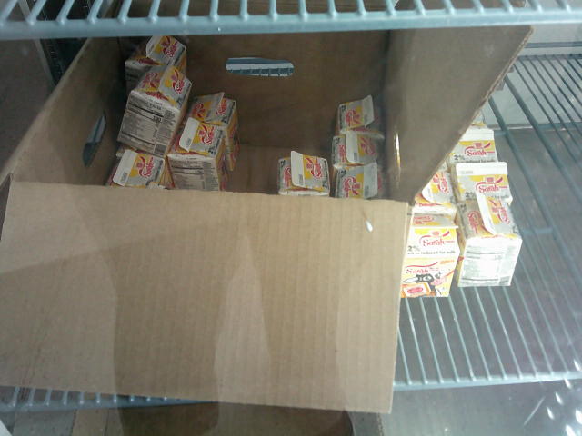 Box of half pint carton milk with some out of the box next to it on the shelf of a fridge.